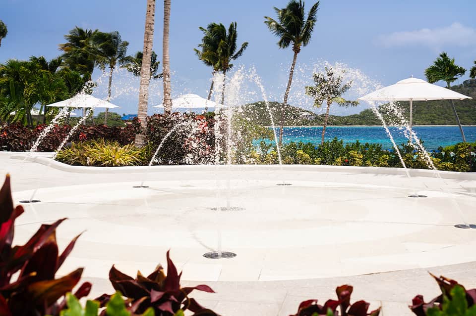 Fountain display on white patio with palm trees, umbrellas, and turquoise ocean view in background