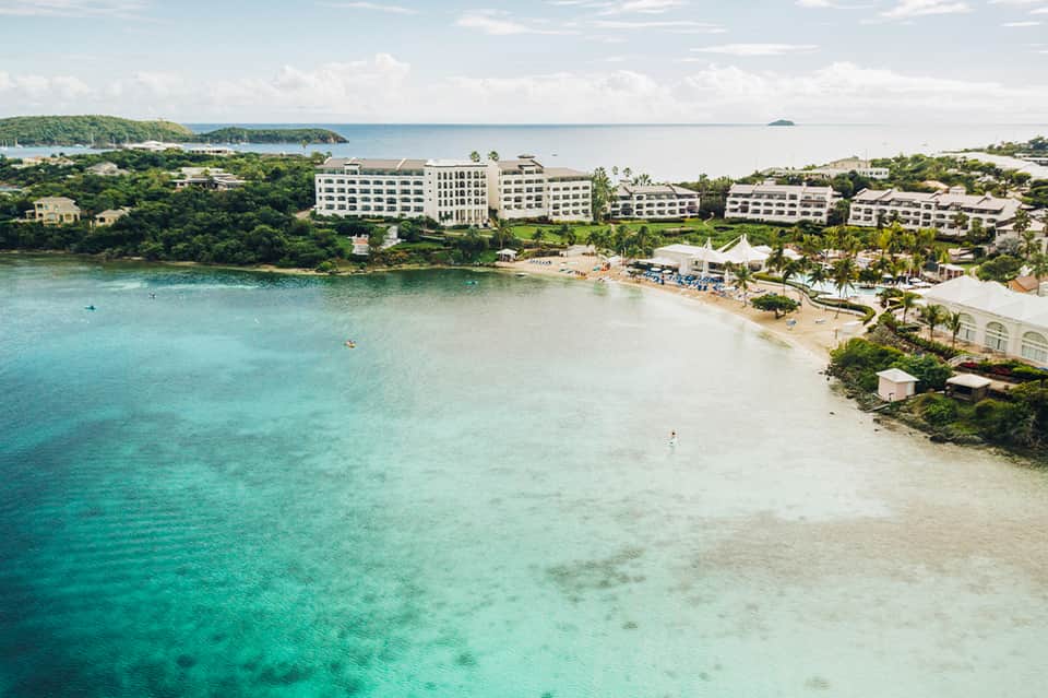 Aerial view of beachfront resort with white buildings, turquoise waters, and sandy beaches