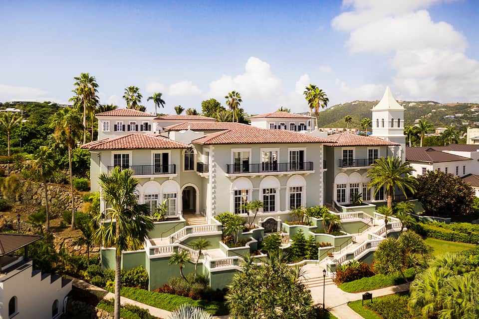 Mediterranean-style white mansion with red tile roof, manicured lawn, and palm trees