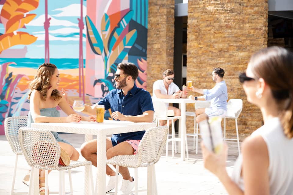 Colorful rooftop bar area with couple dining and vibrant beach mural backdrop