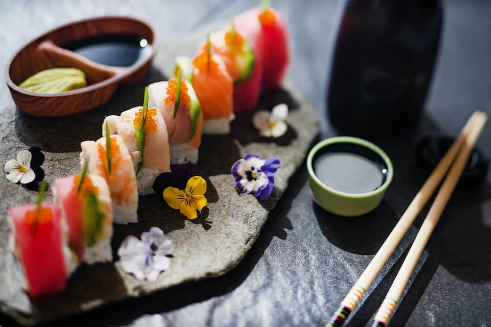 Artfully arranged sushi rolls with edible flowers and condiments on stone slate