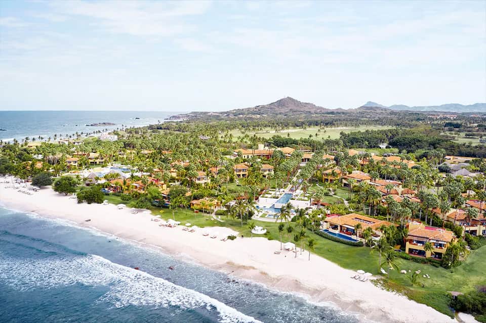 Aerial view of beachfront resort with colorful villas, palm trees, and white sand beach