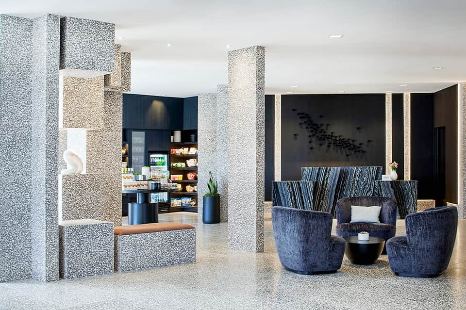 Contemporary hotel lobby with terrazzo columns, blue modern seating, and minimalist design aesthetic