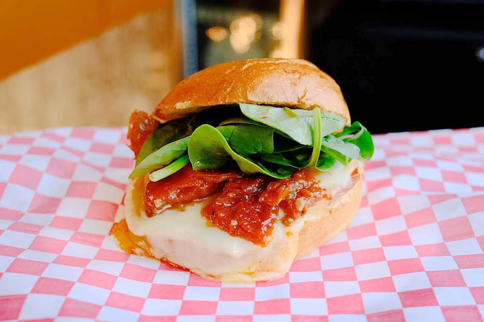 Gourmet burger with tomato sauce, melted cheese, and fresh greens on brioche bun