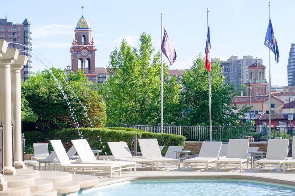 Luxury resort pool area with white loungers overlooking historic church towers and cityscape