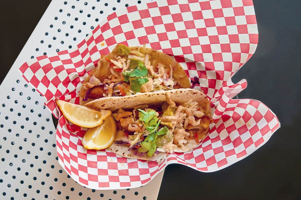 Fish tacos on red and white checkered paper with lemon wedges and fresh cilantro garnish