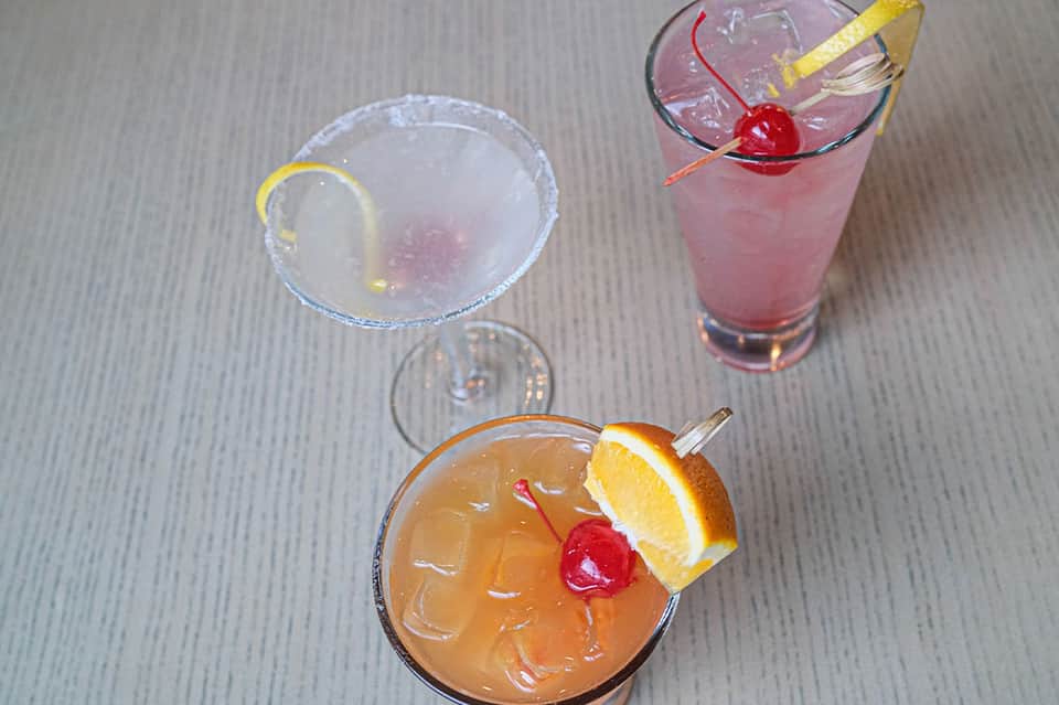Colorful cocktails with citrus garnish and cherry on gray surface