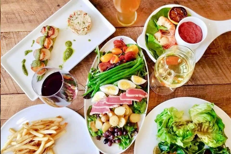 Fine dining presentation with seared scallops, salad, fries, and wine on wooden table
