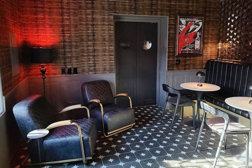 Retro-style lounge with brick walls, red neon lighting, blue velvet seating, and art deco decor