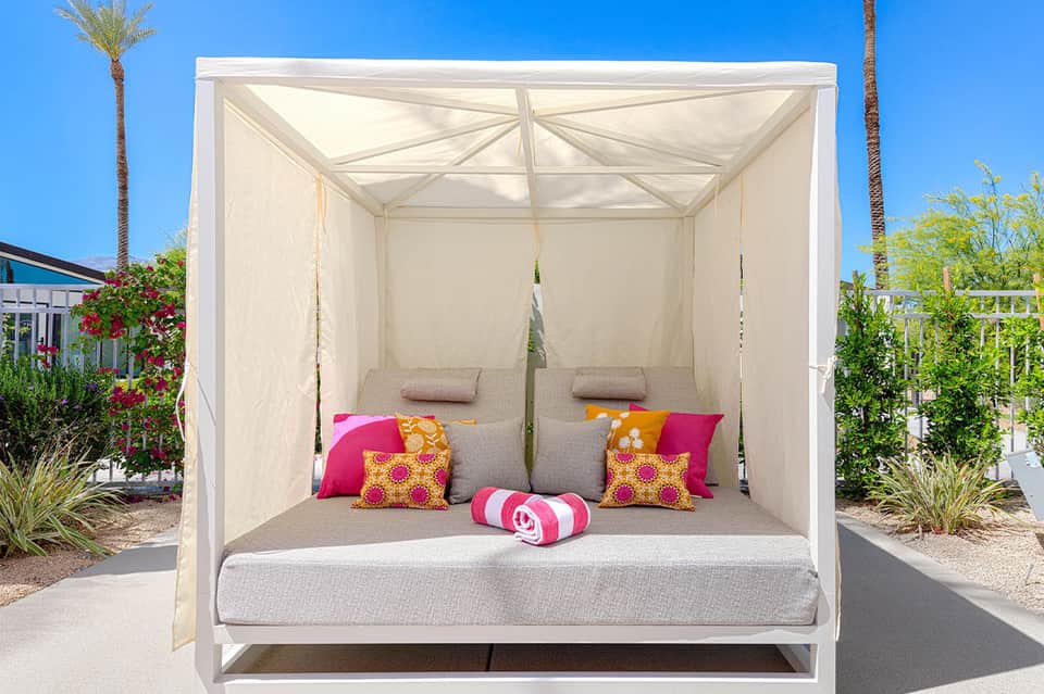White canopy daybed with colorful throw pillows in resort garden with palm trees