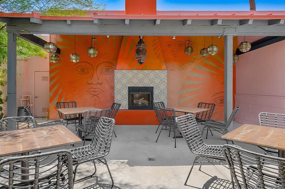 Covered patio with orange mural, fireplace, metal chairs, and hanging lanterns