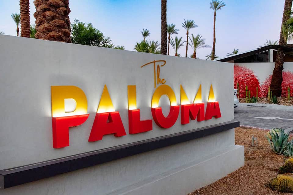 The Paloma resort entrance sign with illuminated yellow and red lettering and palm trees
