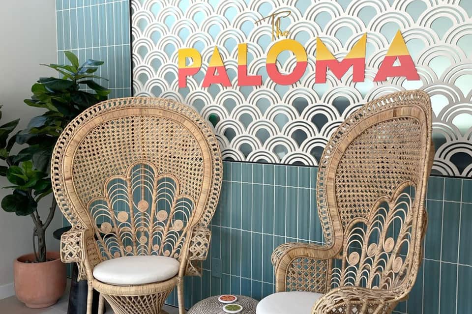 Modern resort lounge area with PALOMA sign, decorative wicker peacock chairs, and geometric wall backdrop