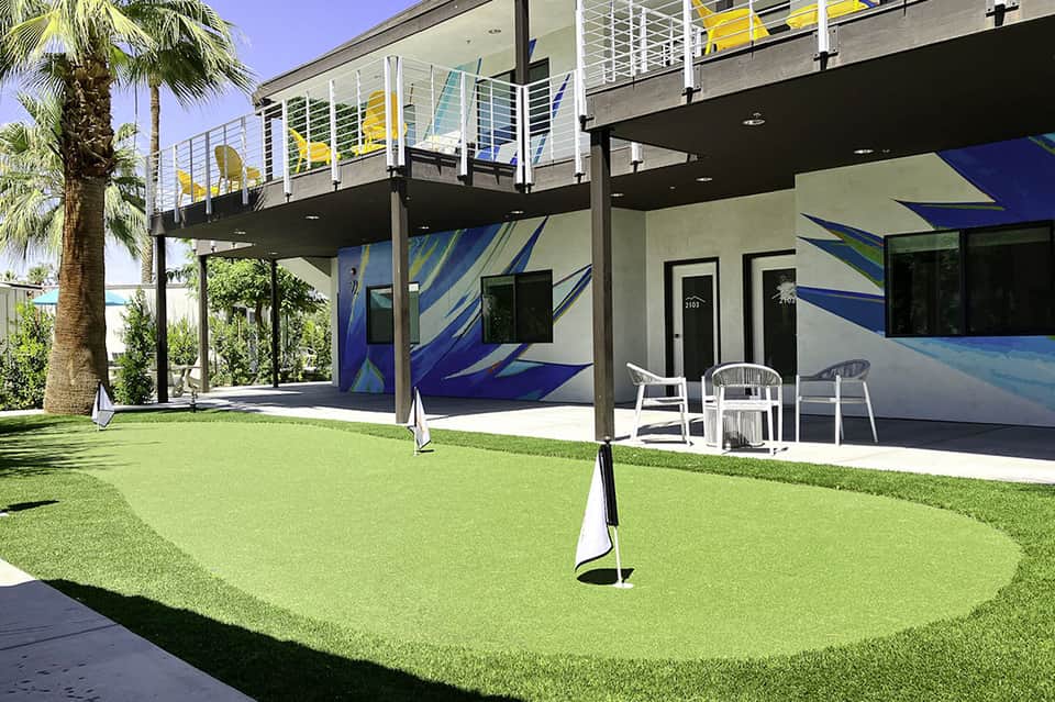 Modern waterfront home with putting green, palm trees, and covered deck area