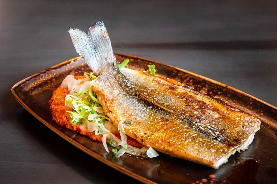 Grilled whole fish fillet with crispy skin garnished with scallions on dark bronze plate