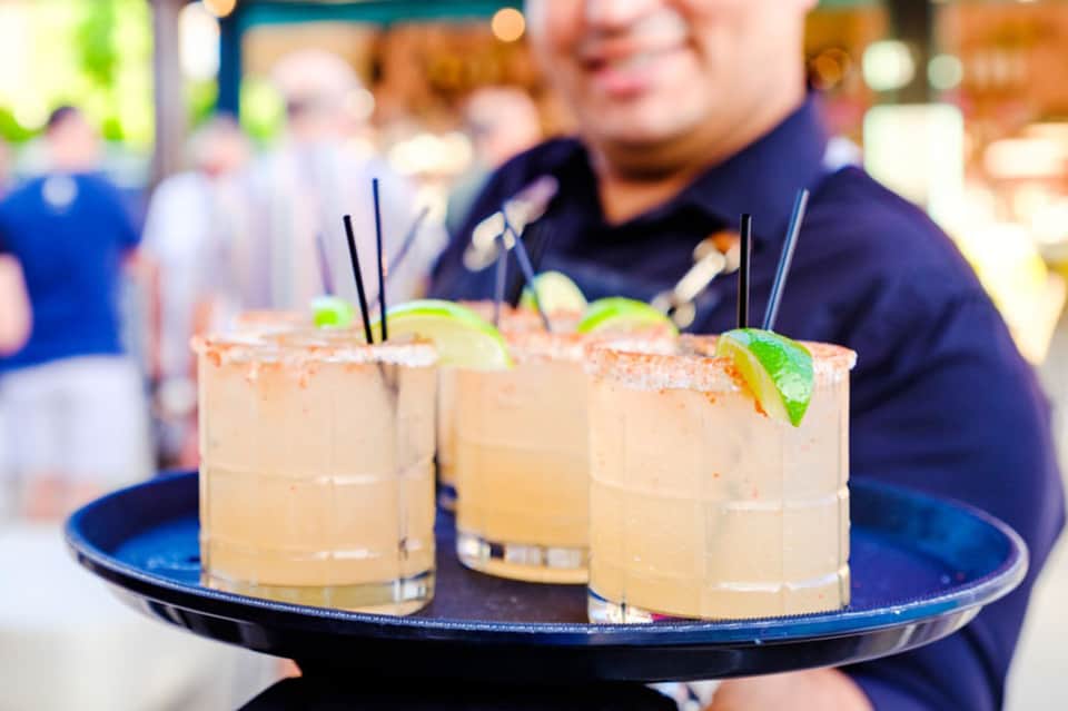 Bartender serving three margarita cocktails with salt rims and lime garnish