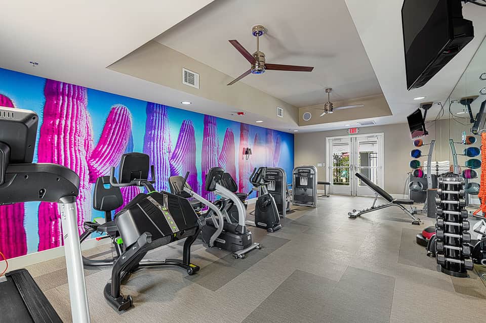 Fitness center with cardio equipment, colorful neon cactus wall mural, weights, and modern amenities