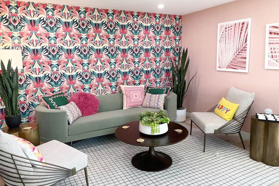 Modern lounge with colorful geometric wallpaper, gray sofa, round black table, and botanical accents