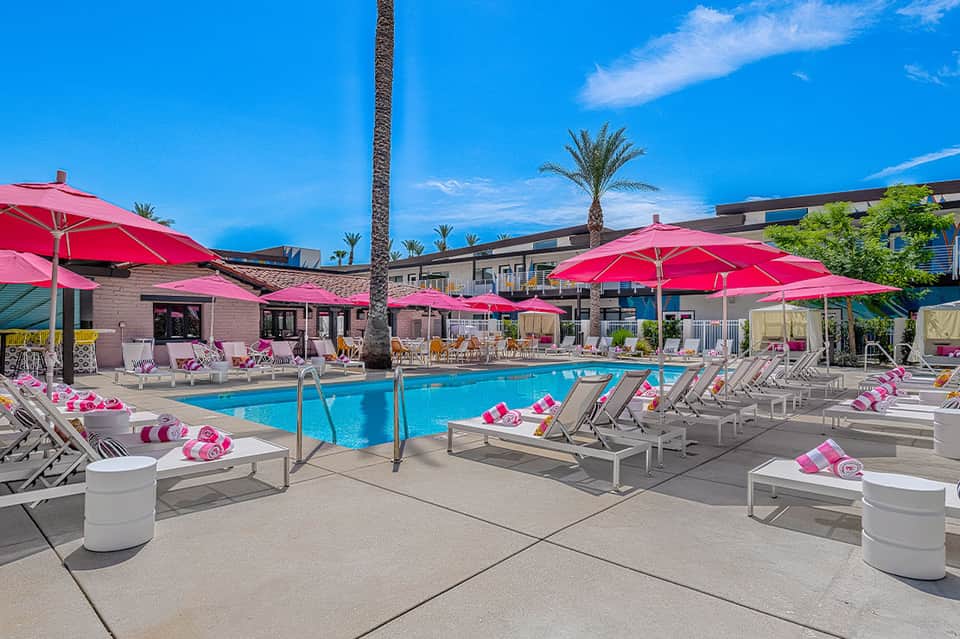 Resort pool with pink umbrellas, lounge chairs, and palm trees under blue sky