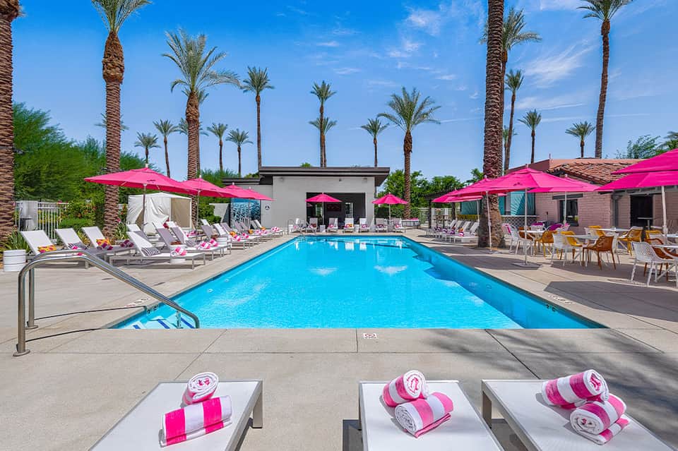 Resort pool with bright pink umbrellas, white loungers, and palm trees under blue sky