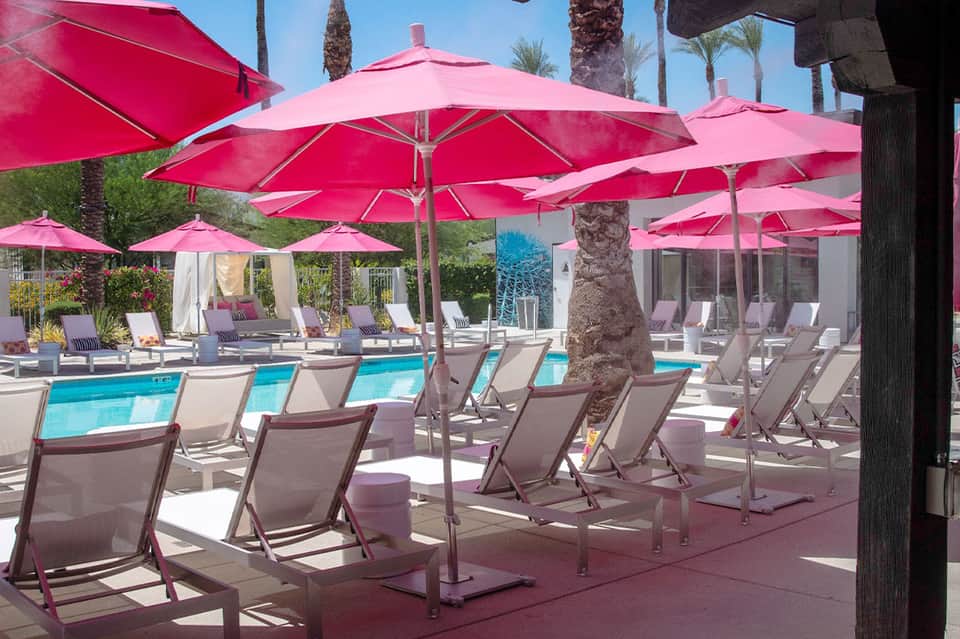 Resort pool area with bright pink umbrellas, beige lounge chairs, and palm trees
