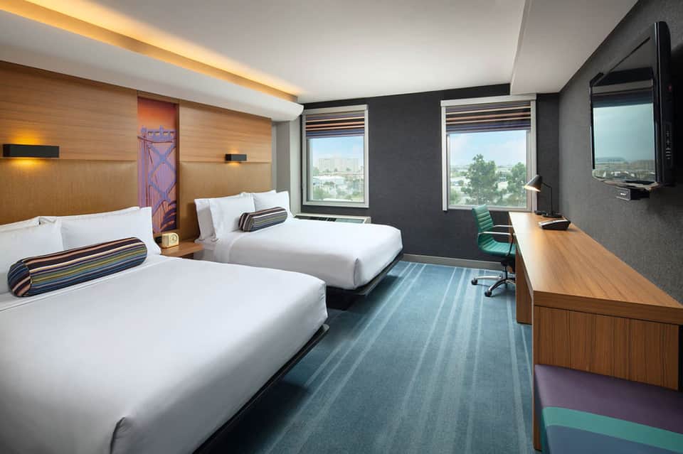 Contemporary hotel room with two beds, wood accents, and city window views