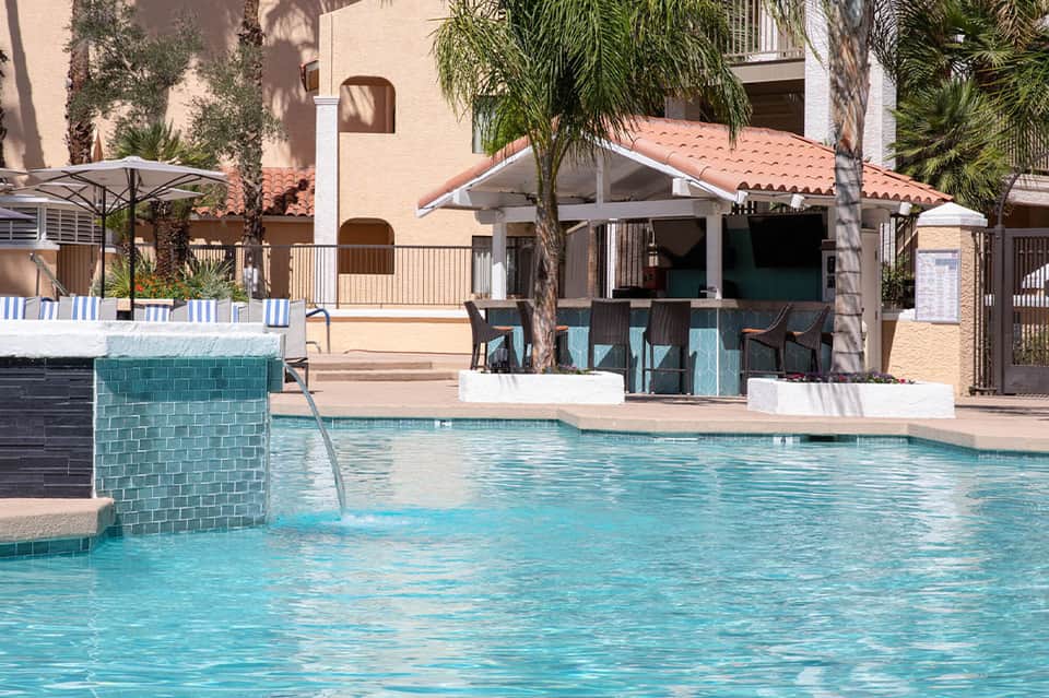 Resort swimming pool with turquoise tile, palm trees, and cabana