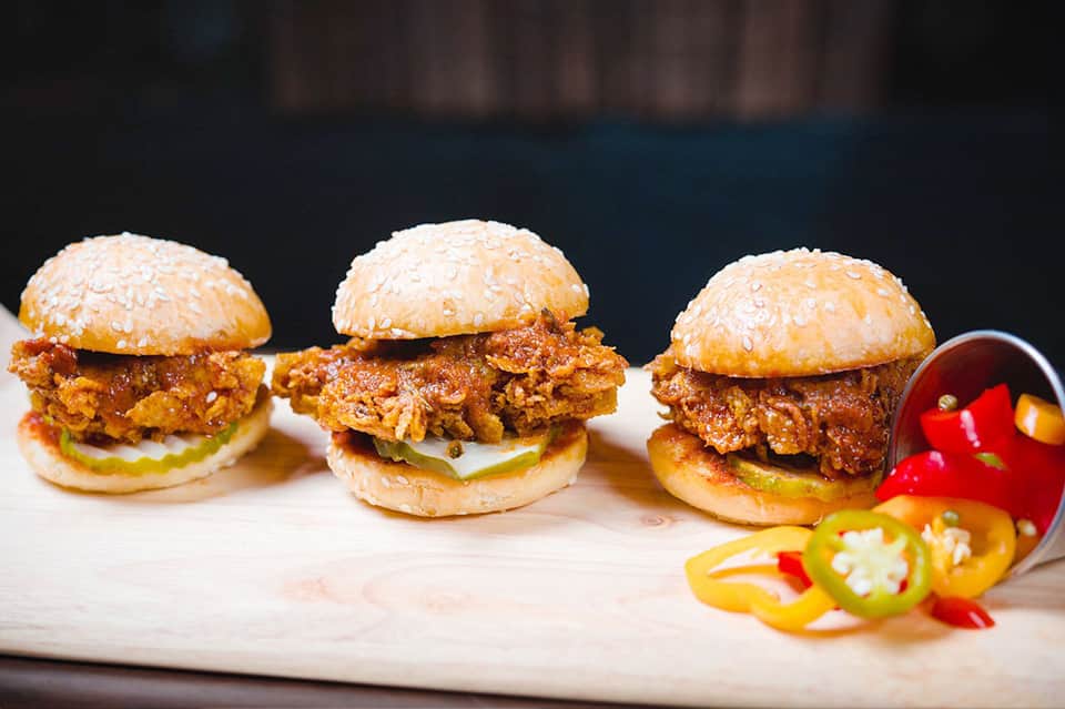 Three crispy fried chicken sliders with sesame buns and jalapeño slices on marble
