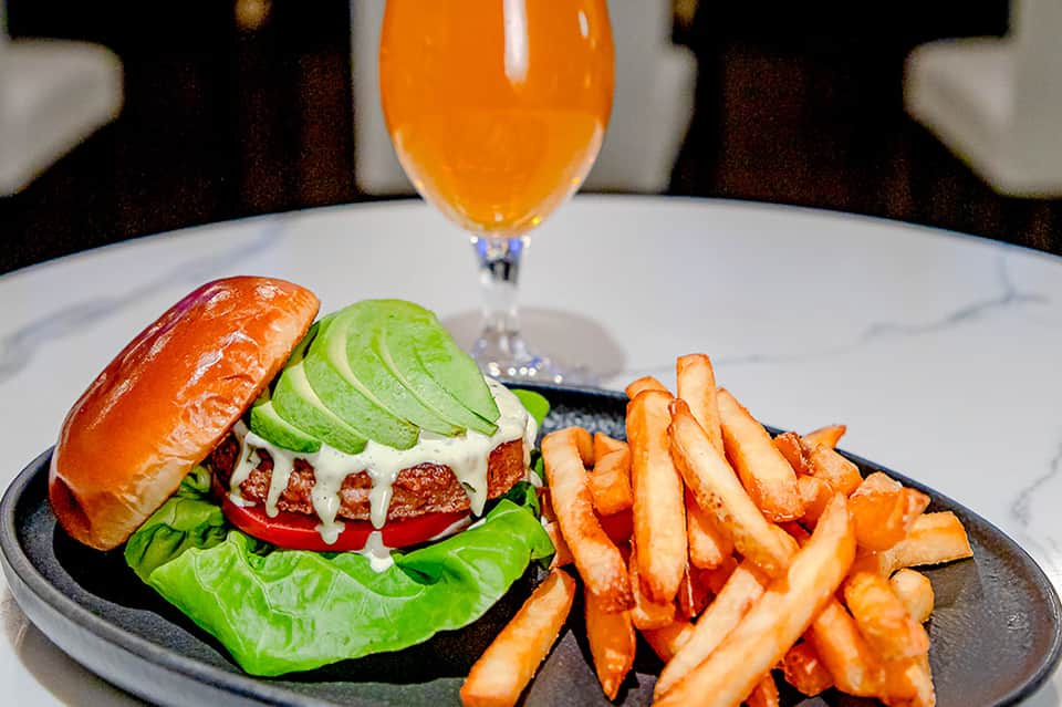 Gourmet burger with avocado slices, melted cheese, fresh greens, and fries served with orange juice