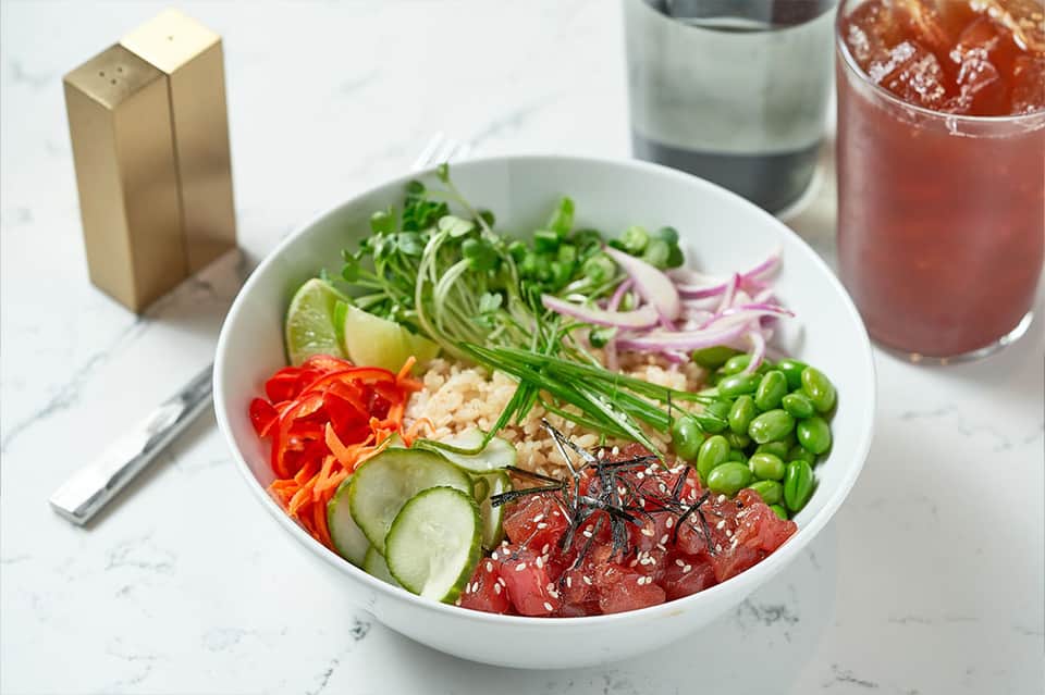 Colorful Asian poke bowl with raw tuna, vegetables, and beverage on marble countertop