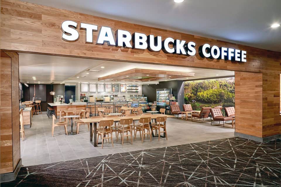Starbucks Coffee storefront with modern wooden design, seating area, and landscape photography backdrop