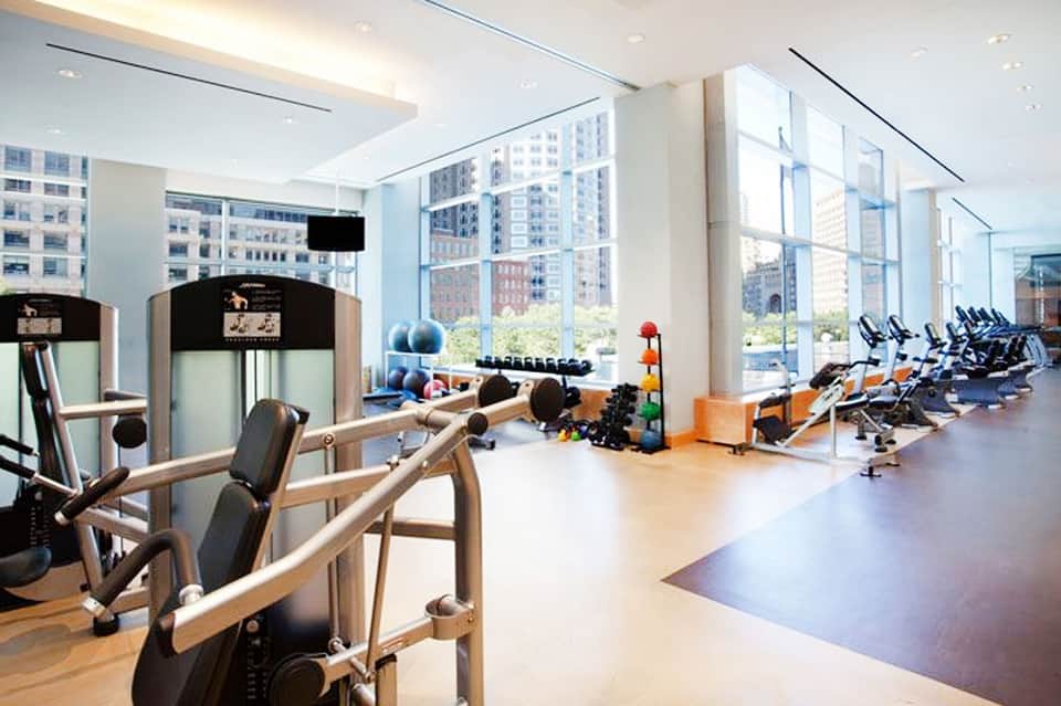 Modern fitness center with floor-to-ceiling windows overlooking city skyline, featuring exercise equipment and stationary bikes