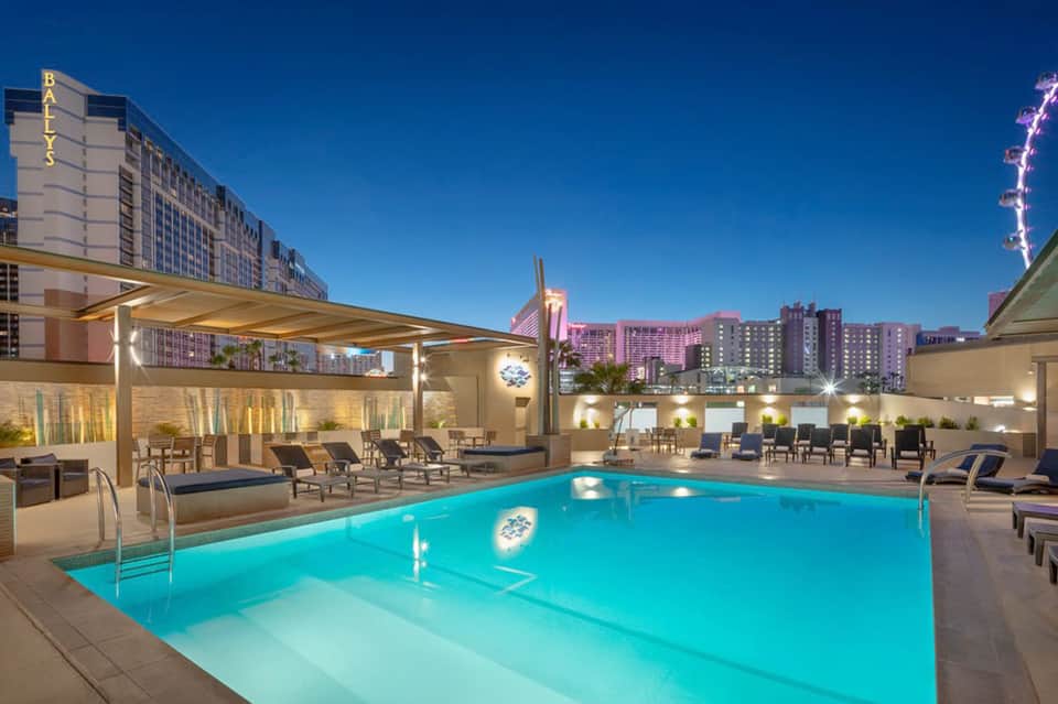 Illuminated rooftop pool at night with lounge chairs and downtown city skyline views
