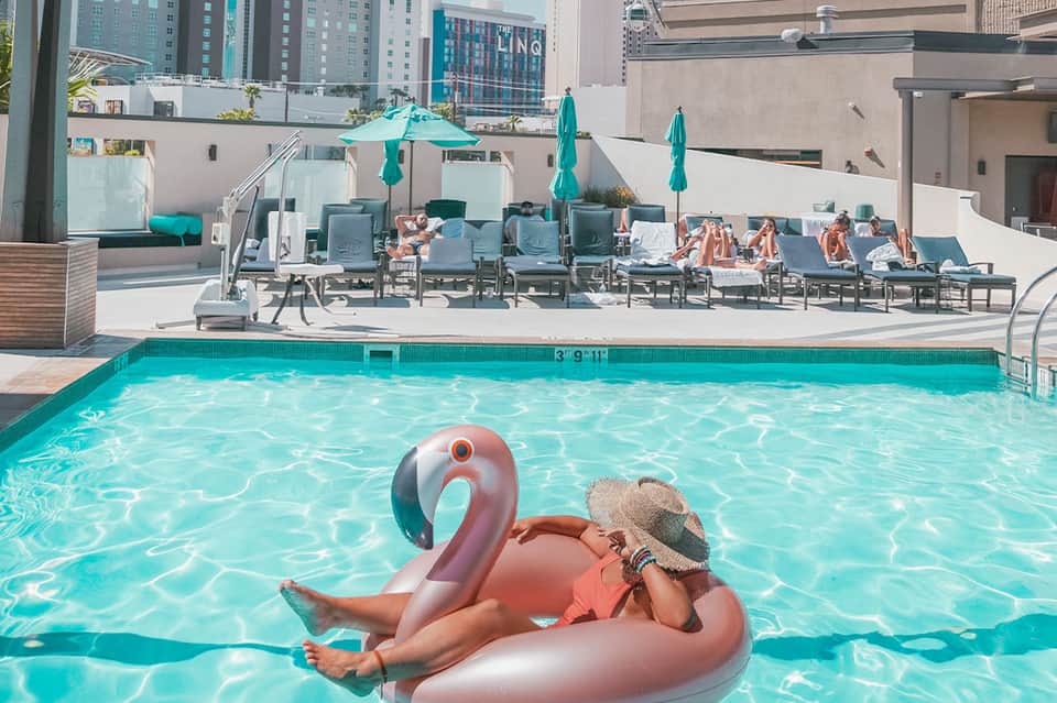 Urban rooftop pool with flamingo float, turquoise water, and downtown city skyline at daytime
