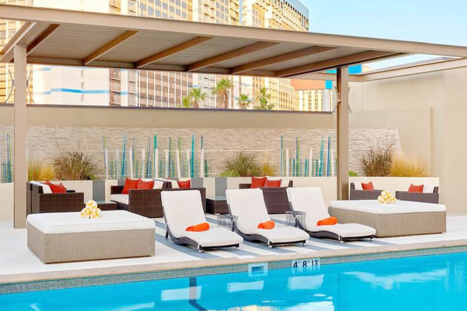 Modern poolside lounge with chaise lounges, pergola shade, and high-rise hotel backdrop