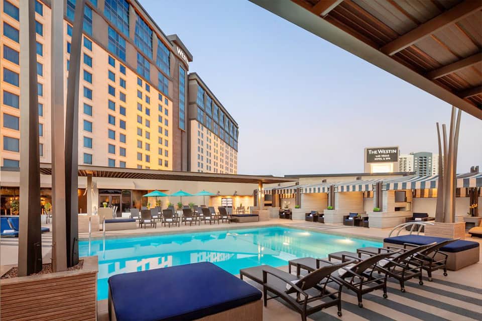 Contemporary resort pool deck with turquoise water, lounge chairs, covered seating areas, and hotel tower