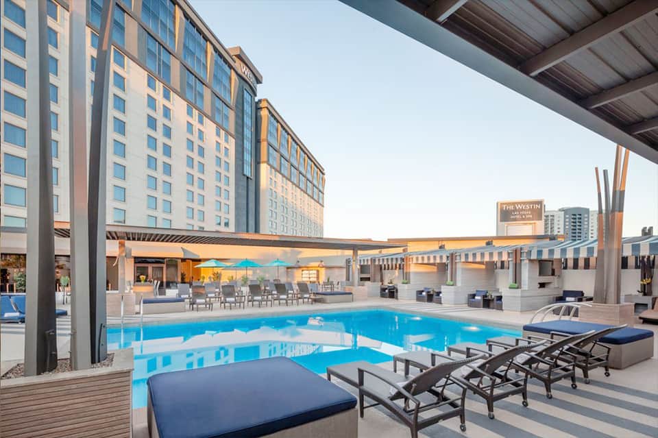Contemporary hotel pool deck at sunset with shade structure, lounge chairs and city skyline