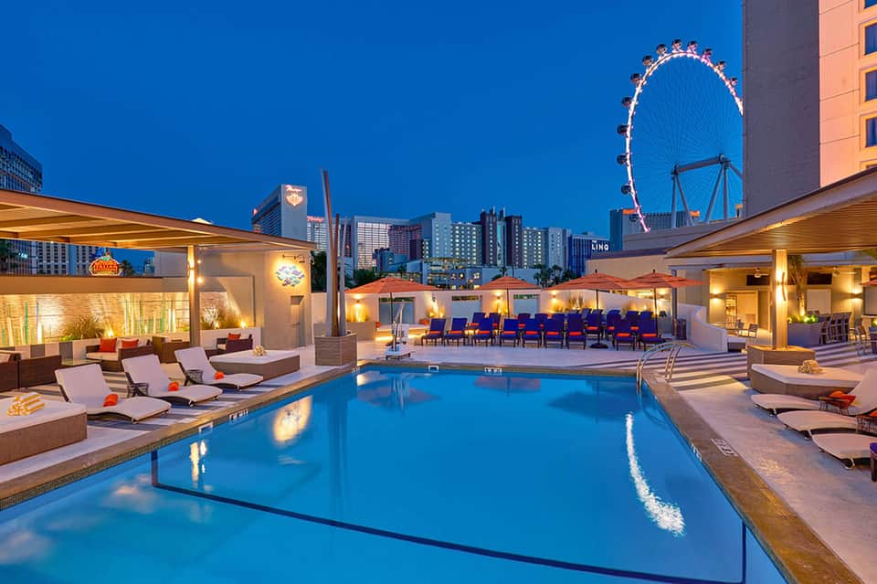 Modern resort pool at night with loungers, the London Eye visible in the background skyline