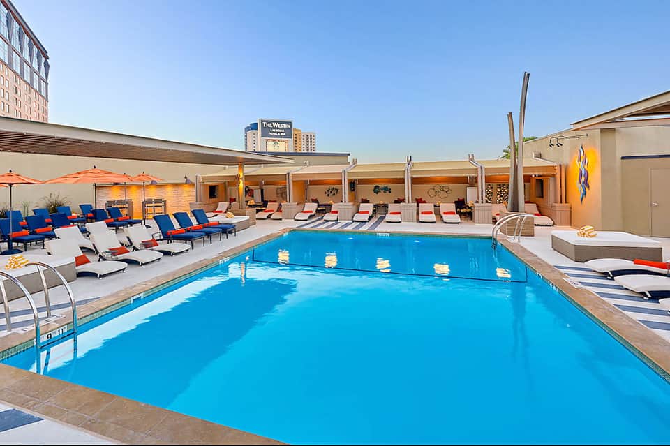 Urban rooftop pool with bright blue water, orange umbrellas, and downtown city skyline