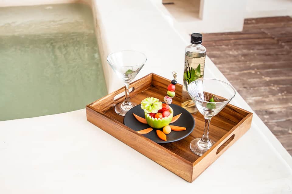 Spa poolside tray with cocktails, decorative fruit plate, and calm water feature in background