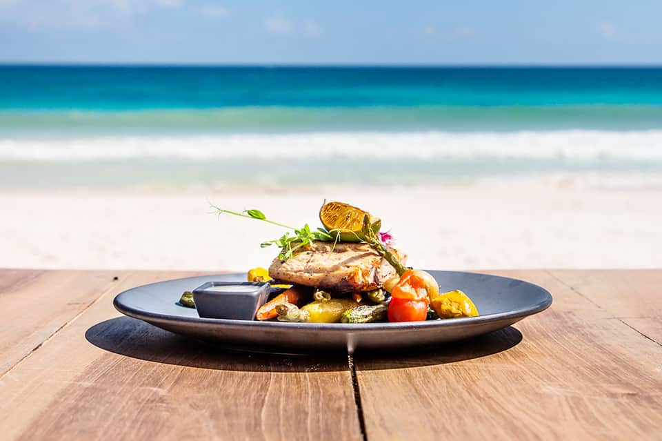 Grilled fish dish with vegetables on dark plate, served beachside with ocean backdrop
