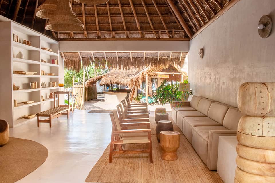 Modern lounge area with thatched ceiling, cream sectional sofa, wooden shelving, and ocean view