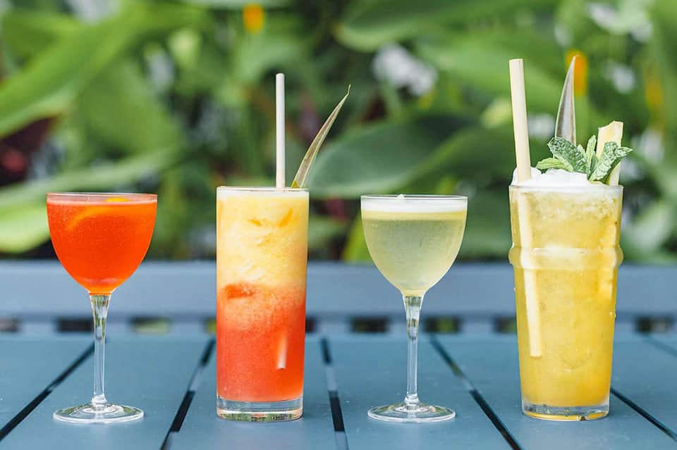 Four colorful cocktails on dark deck with green garden background