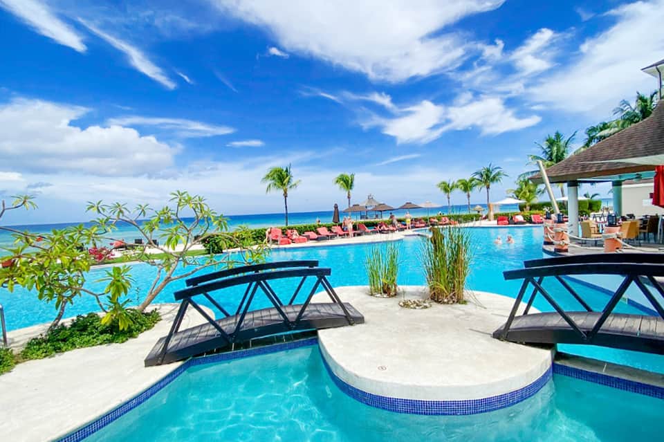 Beachfront resort pool with black lounge chairs, ocean view, and tropical vegetation