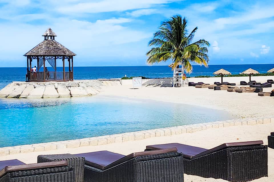 Beach cabana with tiki hut, palm tree, lounge chairs, and turquoise ocean view