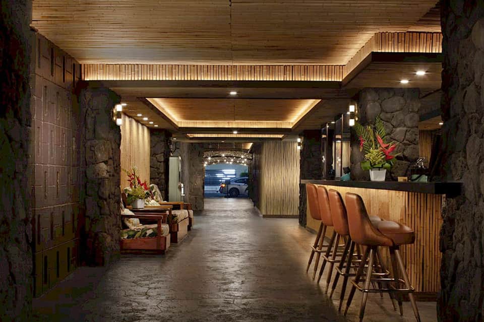 Modern hotel lobby with stone walls, wooden ceiling details, bar seating and ambient lighting
