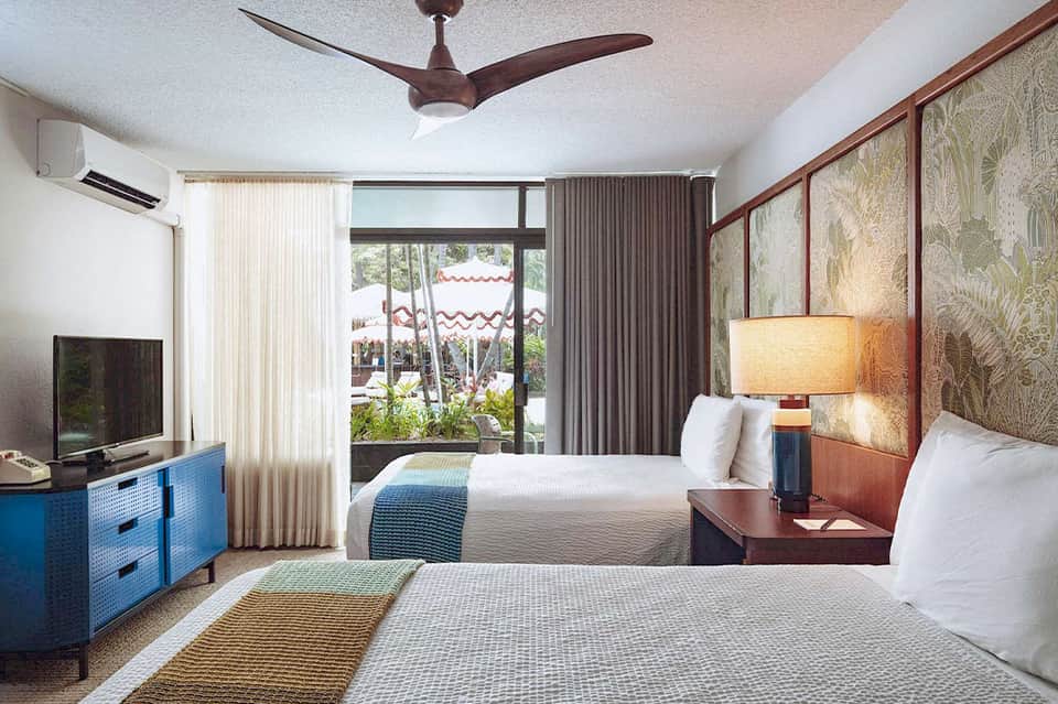 Hotel room with two beds, blue dresser, ocean view balcony, and ceiling fan