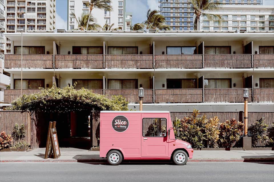 Pink food truck parked in front of modern hotel building with palm trees and residential towers