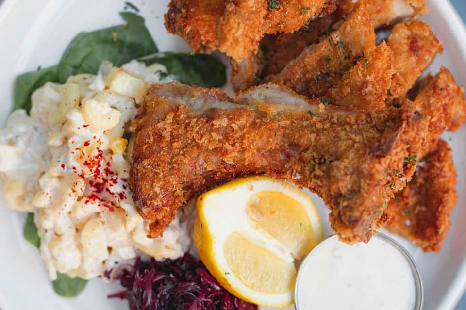 Plated fried chicken with potato salad, beets, lemon, and sauce on white dish