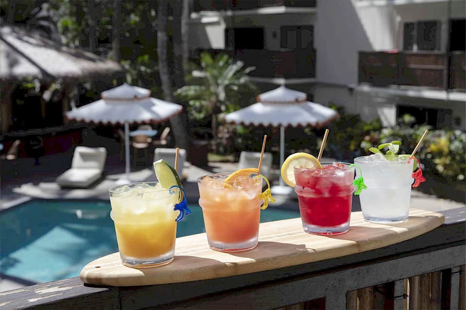 Four colorful tropical cocktails displayed poolside with umbrellas and garnishes